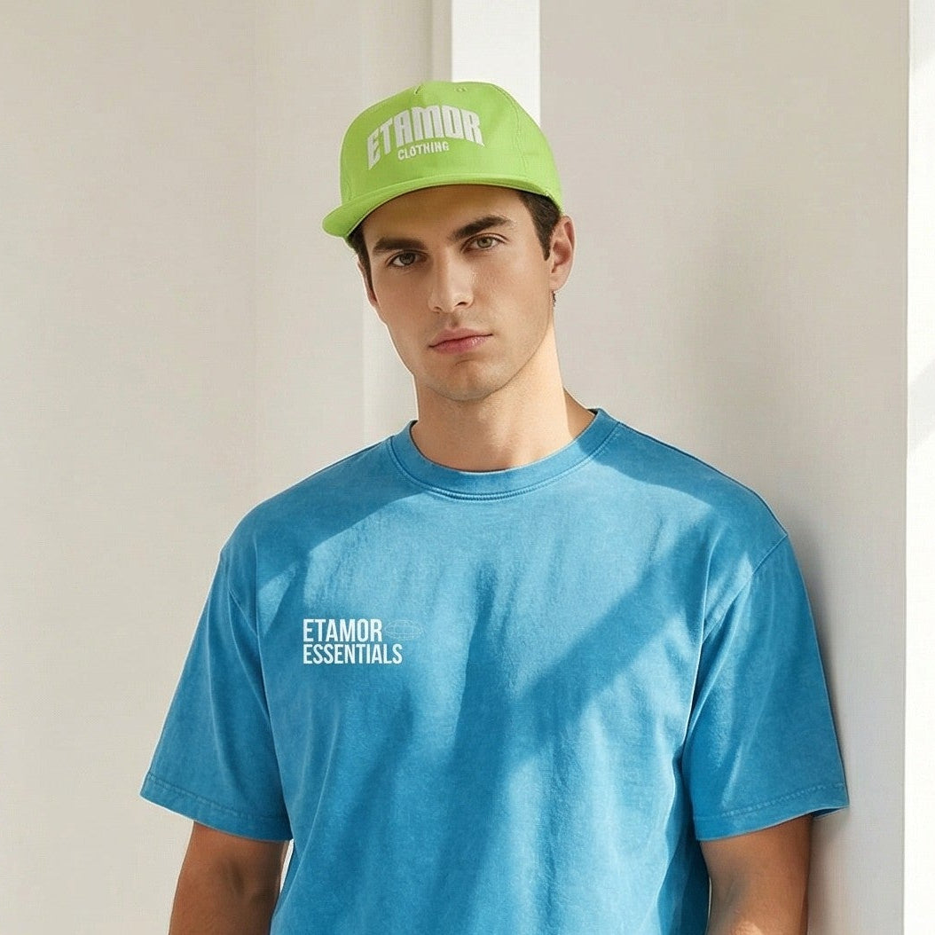 Person wearing a blue t-shirt and beige shorts with a green cap, standing in a bright room.