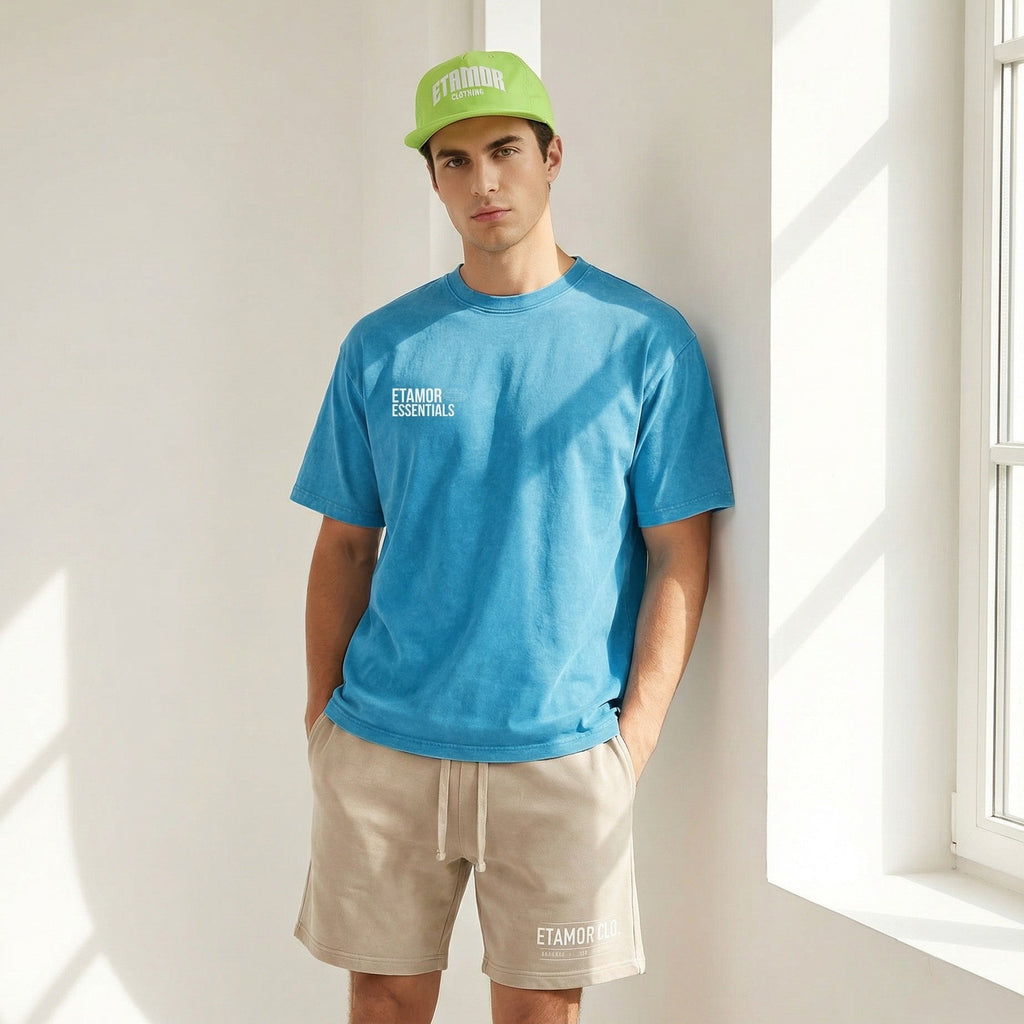 Person wearing a blue t-shirt and beige shorts with a green cap, standing in a bright room.